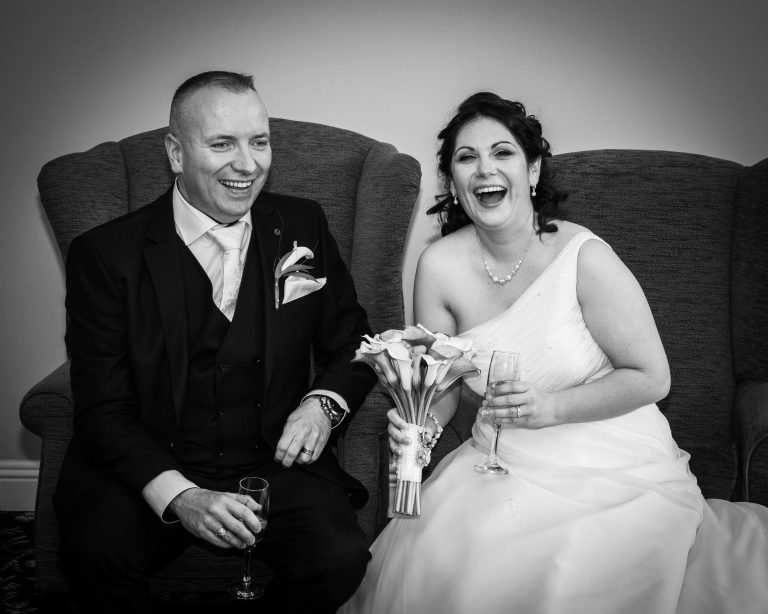 Bride and Groom sitting in big comfortable armchairs, drinking champagne, having a laugh.